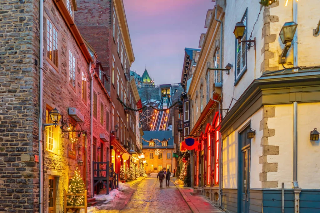 Smalle besneeuwde straat met rode verlichting en versierde gevels leidt naar de toren van Château Frontenac in Québec City