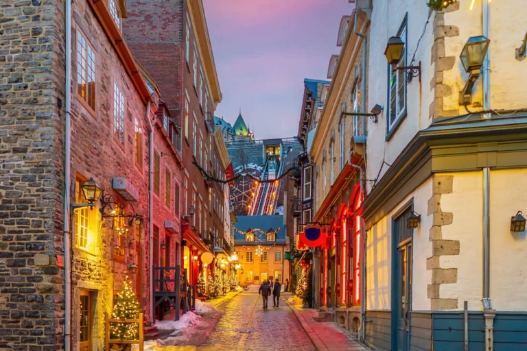 Smalle besneeuwde straat met rode verlichting en versierde gevels leidt naar de toren van Château Frontenac in Québec City