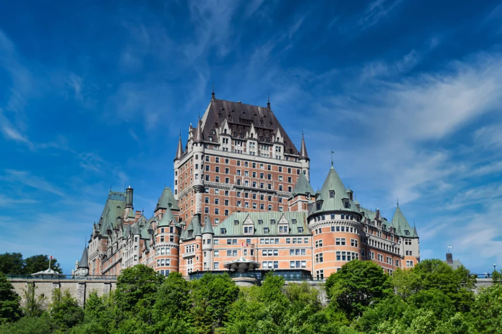 Het kasteelachtige hotel Château Frontenac met groene torenspitsen boven groen geboomte, gefotografeerd onder een strakblauwe hemel in Quebec City