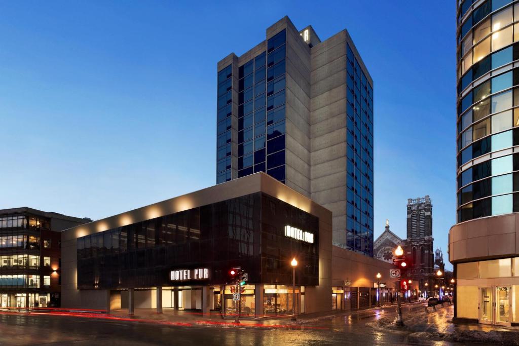 Modern hoog hotelgebouw op een straathoek met verlichte gevel, met op de achtergrond de torenspitsen van een kathedraal in Quebec City