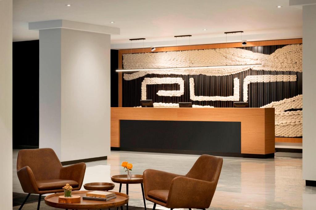 Moderne hotellobby met de naam PUR op de wand achter de balie en bruine leren fauteuils op de voorgrond in Quebec City
