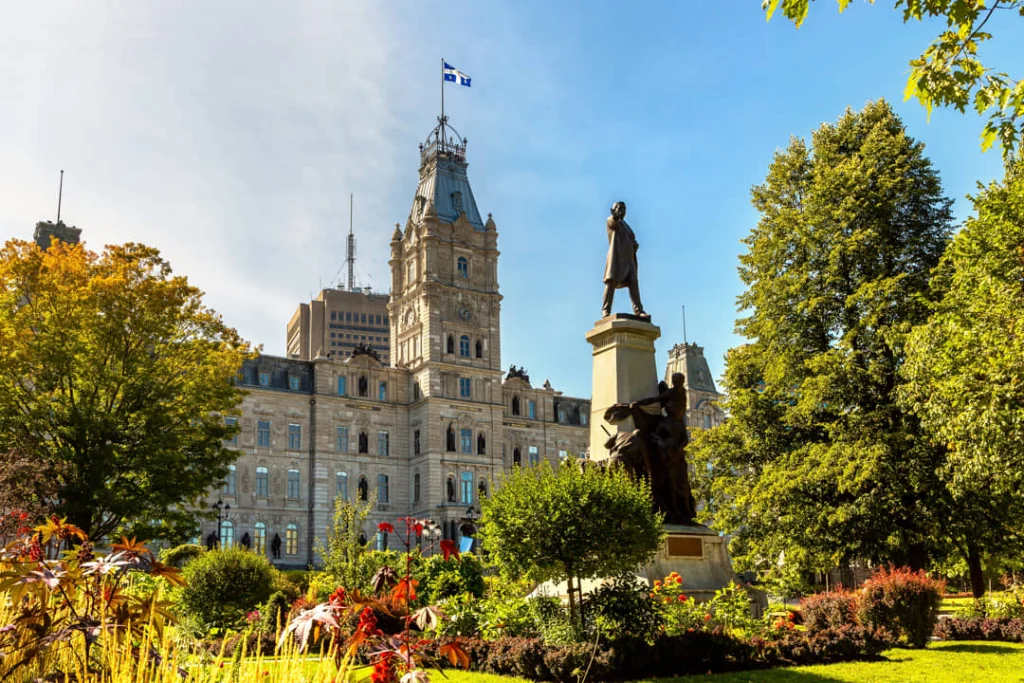 Het historische parlementsgebouw van Québec met een torenspits en een standbeeld tussen bloemperken in een park