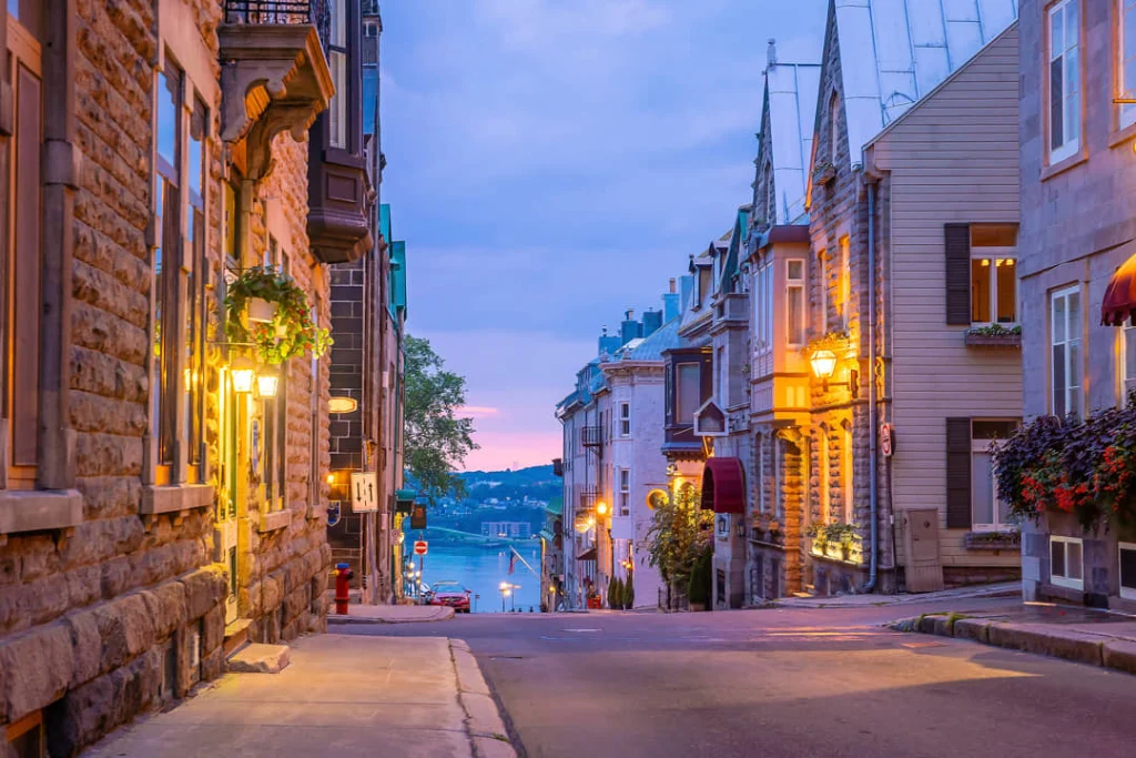 Verlichte straatlantaarns langs een aflopende straat in Québec City met uitzicht op de rivier bij schemering