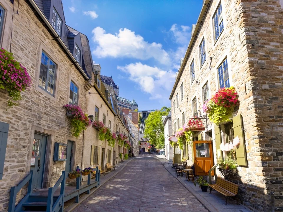 Smal geplaveid straatje met stenen huizen vol bloembakken en op de achtergrond de torens van Château Frontenac