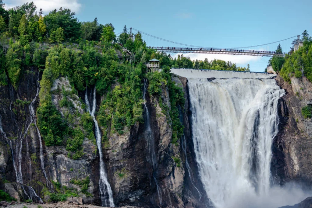 Een hangbrug met bezoekers overspant de top van de Montmorency waterval die tussen groene kliffen naar beneden stort