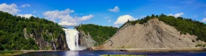 Brede waterval die tussen beboste kliffen naar beneden stort met een rivier eronder in de omgeving van Québec