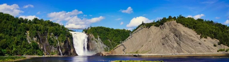 Brede waterval die tussen beboste kliffen naar beneden stort met een rivier eronder in de omgeving van Québec