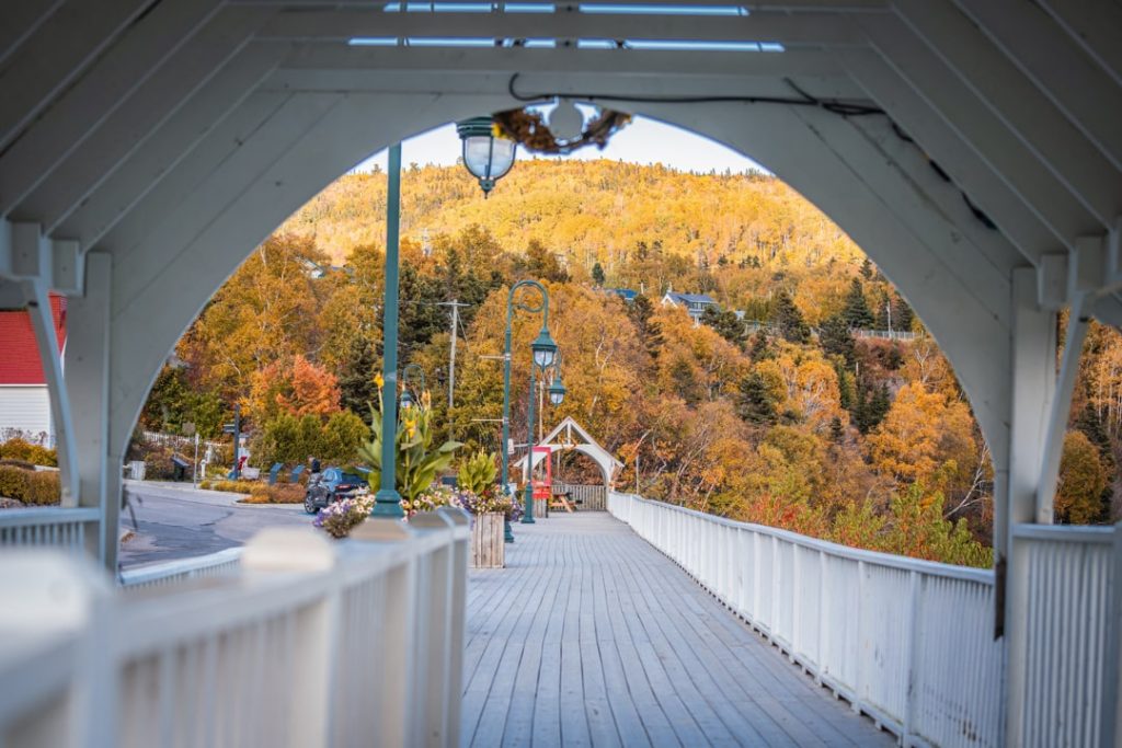 Uitzicht door de boog van een overdekte houten voetgangersbrug op een straat en een heuvel vol herfstkleuren