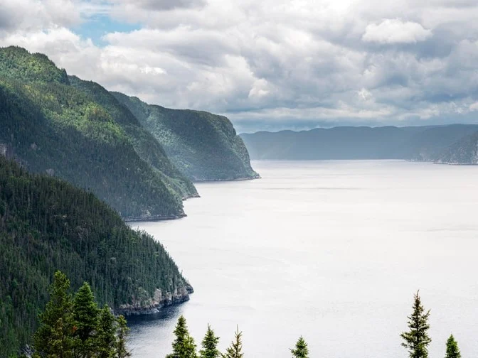 Weids uitzicht over de Saguenay fjord met steile groene kliffen aan weerszijden van kalm water onder bewolkte lucht