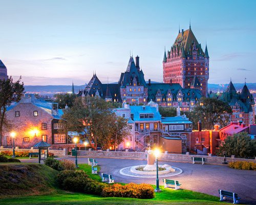 Historisch stadsplein met verlichte lantaarns en bankjes voor het kasteelhotel Chateau Frontenac in Quebec Stad bij zonsondergang