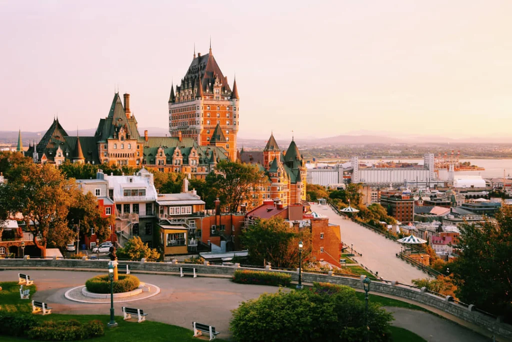 Uitzicht op hotel Château Frontenac met zijn torens tegen een roze avondlucht, met de rivier op de achtergrond