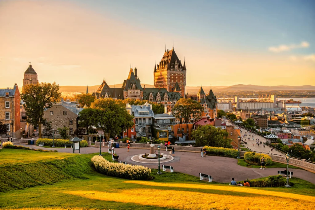 Château Frontenac gezien vanaf een groen plein met wandelaars, badend in het gouden licht van de zonsondergang