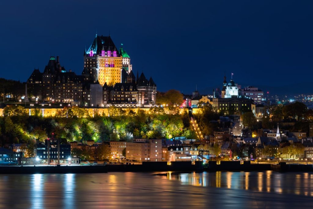 Nachtelijk uitzicht vanaf het water op het verlichte Chateau Frontenac hoog op de klif boven de rivier in Quebec Stad met lichtjes die weerspiegelen in het water