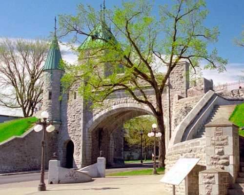 Stenen stadspoort met groene torenspitsen en een trap ernaast in de ommuurde oude binnenstad van Quebec Stad