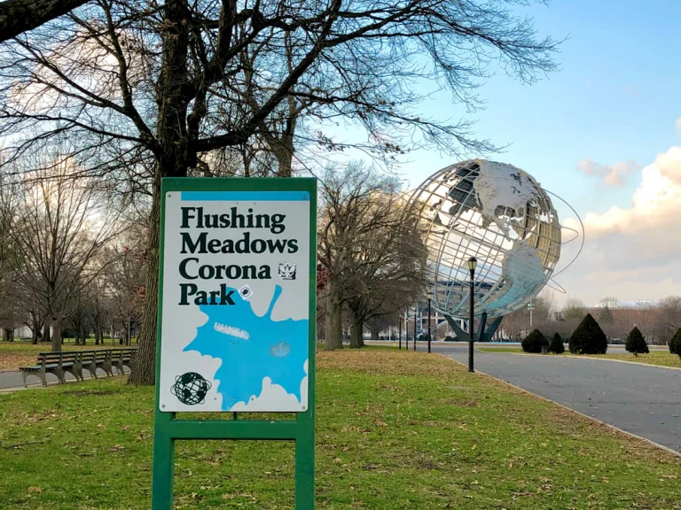 Groen informatiebord met de tekst Flushing Meadows Corona Park, met de metalen Unisphere op de achtergrond tussen kale winterbomen