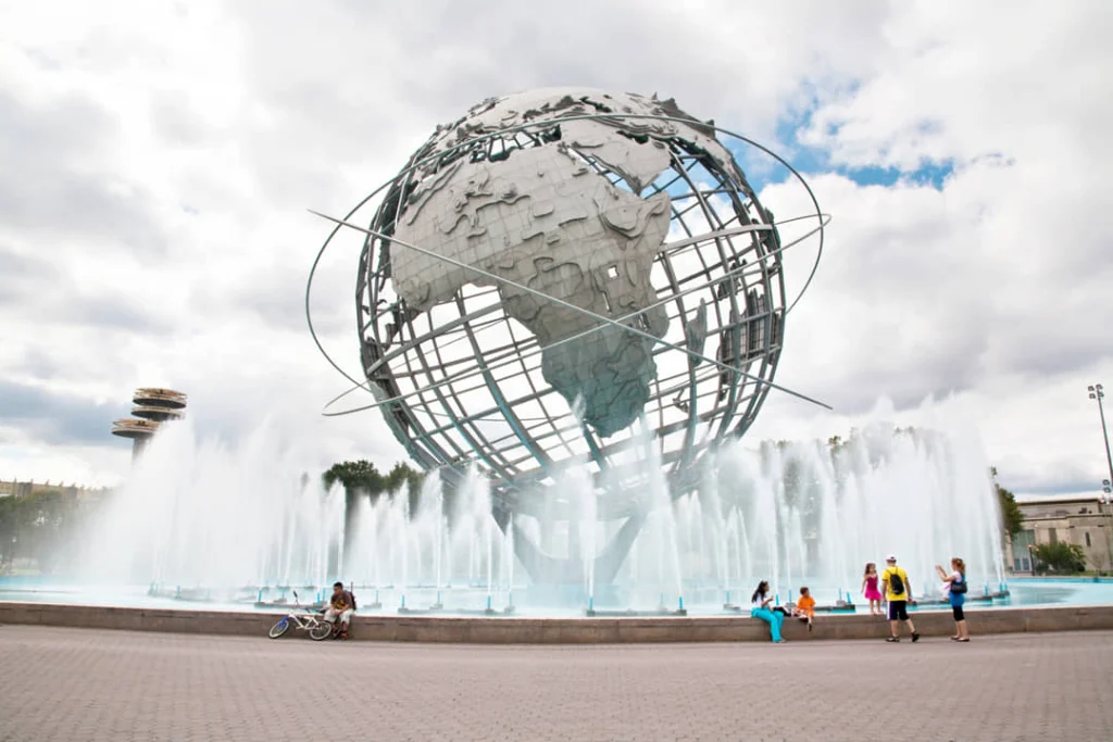 De grote metalen wereldbol Unisphere omringd door spuitende fonteinen in Flushing Meadows Corona Park in Queens, met bezoekers eromheen