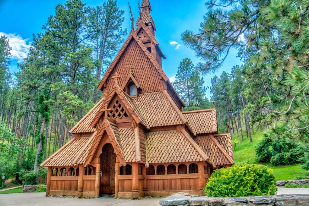 Houten kerk met stavkerkarchitectuur en puntige daken omgeven door dennenbomen en groen gras