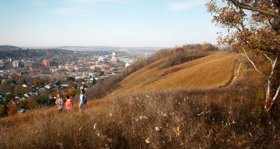 Drie wandelaars lopen over een graspad op Barn Bluff, met de stad Red Wing en de rivier op de achtergrond