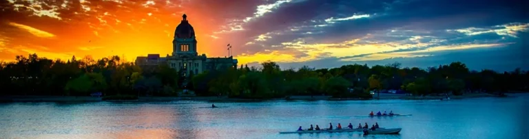 Silhouet van de koepel van het Saskatchewan Legislative Building in Regina tegen een felrode avondlucht met roeiers op Wascana Lake op de voorgrond