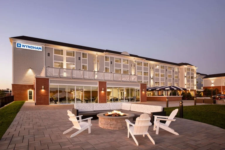 Wit hotelgebouw van Wyndham met verlichte ramen en een terras met witte stoelen rond een vuurkorf bij schemering in Rhode Island
