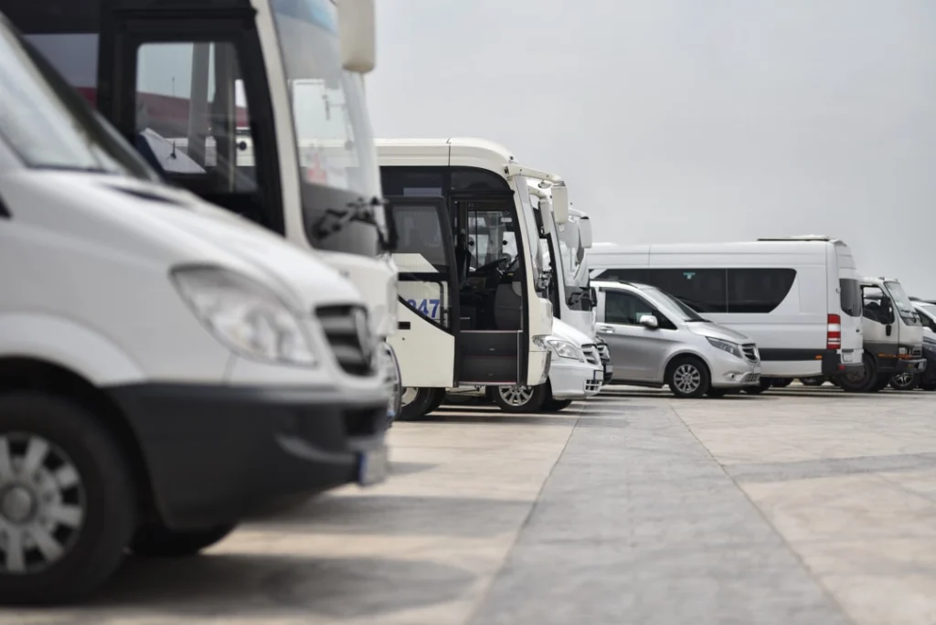 Een rij witte touringcars en busjes staat geparkeerd op een parkeerplaats, klaar voor een transfer tussen hotel en luchthaven