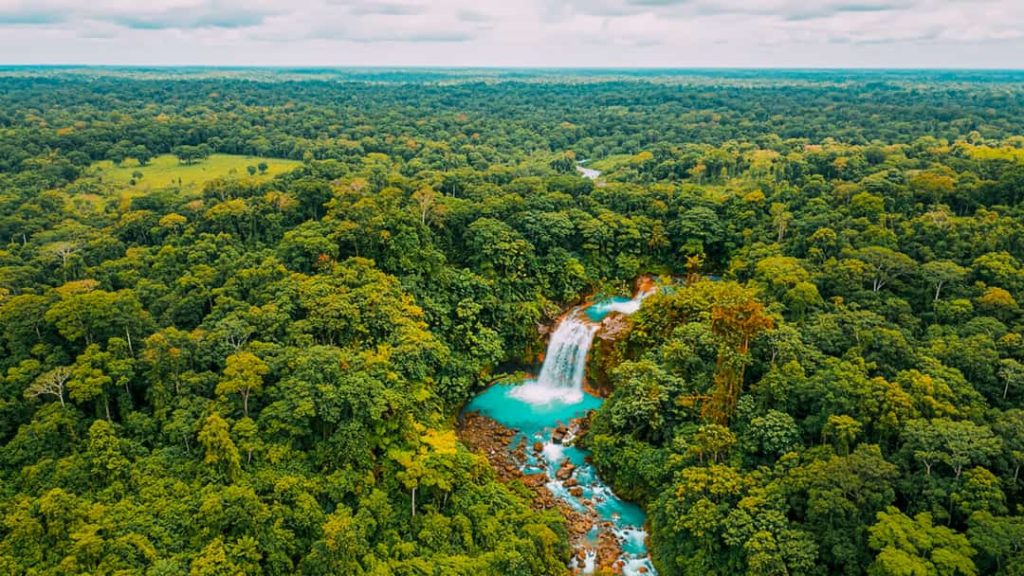 Luchtfoto van een turkooize rivier en waterval die door een uitgestrekt groen regenwoud slingert bij Rio Celeste in Costa Rica