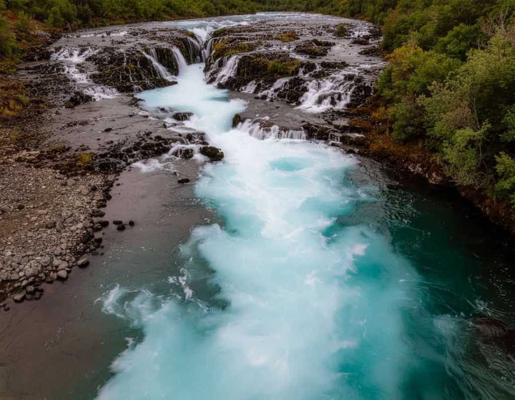 Twee waterstromen komen samen over rotsen, waarbij het water door een natuurlijk proces een felle turkooise kleur krijgt bij Rio Celeste in Costa Rica