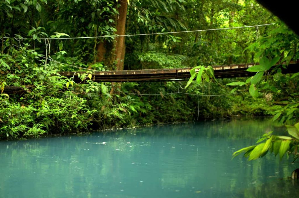 Smalle houten loopbrug aan touwen gespannen over een turkooize kreek in het regenwoud bij Rio Celeste in Costa Rica