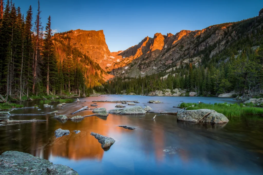 Bergtoppen rond Dream Lake in Rocky Mountain National Park kleuren oranje in het ochtendlicht terwijl rotsen uit het heldere meer steken