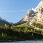 Kronkelende bergweg met haarspeldbochten klimt tegen een steile rotsachtige berghelling boven een turkooizen rivier