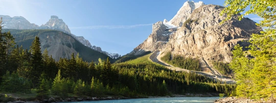 Kronkelende bergweg met haarspeldbochten klimt tegen een steile rotsachtige berghelling boven een turkooizen rivier