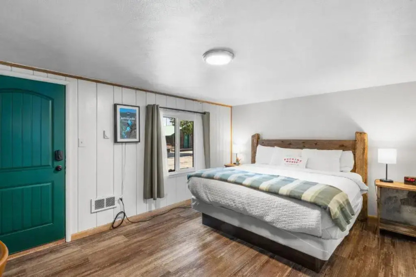 Slaapkamer met een tweepersoonsbed, houten wanden, een groene deur en een raam met uitzicht naar buiten in een rustieke blokhut