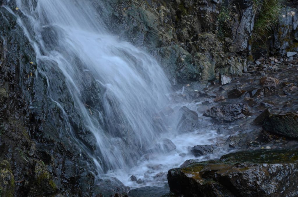 Close-up van een waterval die over donkere, met mos begroeide rotsen stroomt in een schaduwrijke kloof