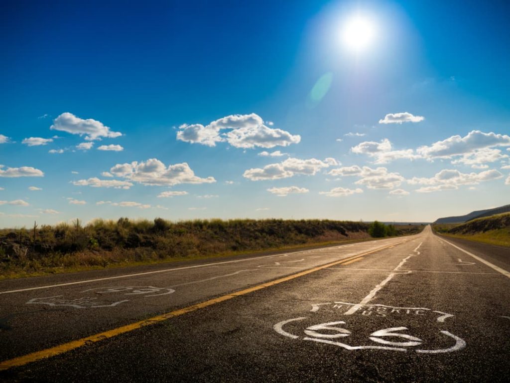 Geschilderde Route 66 tekens op het asfalt van een verlaten tweebaansweg die zich uitstrekt door een droog woestijnlandschap onder een zonnige hemel