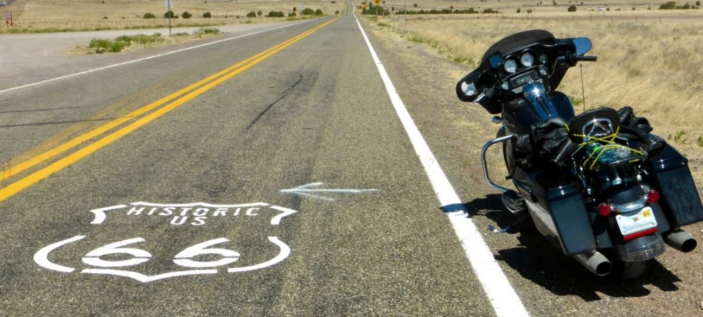 Geschilderd Route 66 schild op een lege asfaltweg door een droog landschap met een zwarte tourmotor geparkeerd langs de wegrand