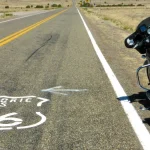 Geschilderd Route 66 schild op een lege asfaltweg door een droog landschap met een zwarte tourmotor geparkeerd langs de wegrand