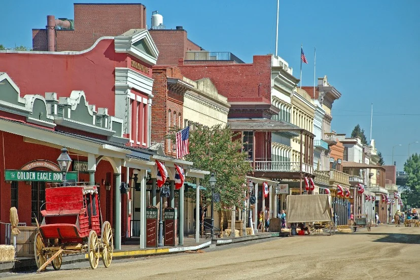 Rij historische negentiende-eeuwse gebouwen met een oude huifkar aan een onverharde straat in Old Sacramento