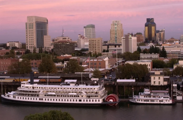 Skyline van Sacramento kleurt roze in de avondschemering, met twee historische raderboten afgemeerd aan de rivier