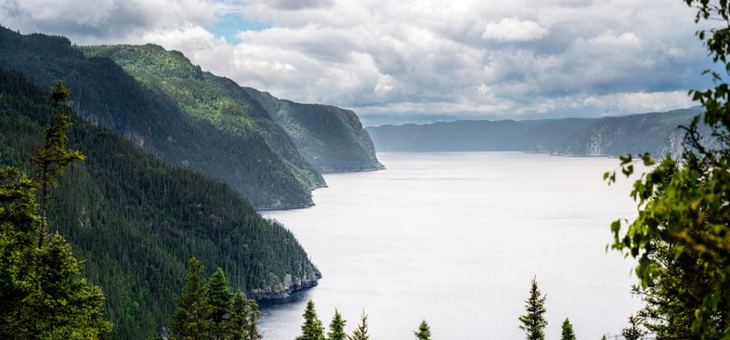 Brede fjord met steile beboste oevers strekt zich uit onder een bewolkte hemel in de Saguenay