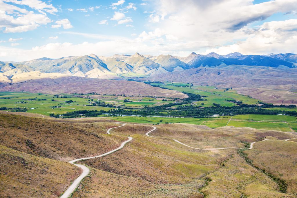 Panoramisch uitzicht vanaf een heuvel over een groen rivierdal met kronkelende weg en een indrukwekkende bergketen op de achtergrond