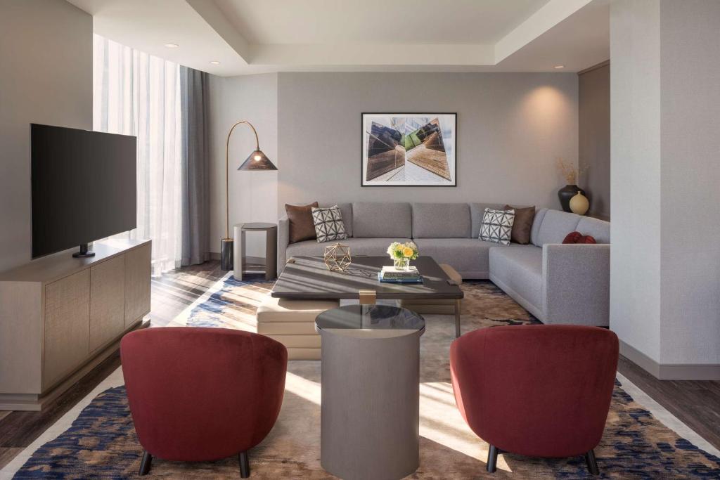 Een moderne hotellounge met een grijze bank, twee rode fauteuils en een salontafel op een patroontapijt