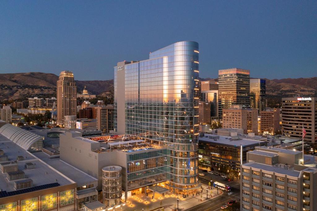 Een hoge glazen hoteltoren staat tussen de skyline van Salt Lake City met bergen op de achtergrond bij avondlicht