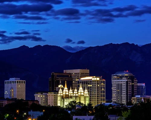 Verlichte wolkenkrabbers en de spitse torens van de tempel in het centrum van Salt Lake City tegen bergen bij nacht
