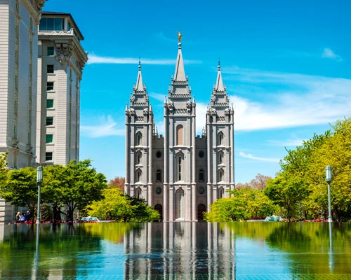 Witte tempel met spitse torens weerspiegeld in een rustige vijver, omringd door groene bomen onder een blauwe lucht