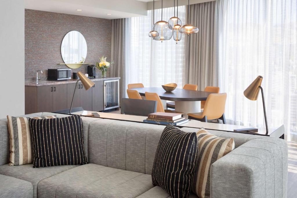 Een ruime hotelsuite met een grijze bank, ronde tafel en eethoek met stoelen bij een hotel in Salt Lake City