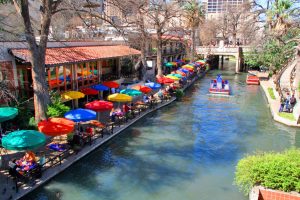 Terrassen met kleurrijke parasols langs het kanaal van de River Walk in San Antonio, met toeristenboten op het water