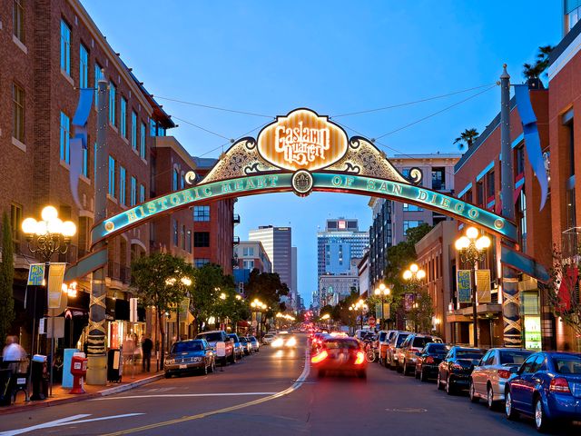 Sierlijke verlichte boog met de tekst Gaslamp Quarter Historic Heart of San Diego boven een drukke straat met auto's en verlichte gevels