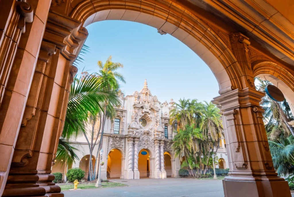 Uitzicht door een stenen boog op een sierlijk versierd gebouw met palmbomen in Balboa Park in San Diego
