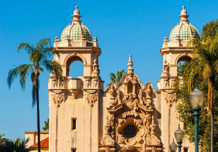 Twee decoratieve torens met groen geblokte koepeldaken van een koloniaal gebouw in Balboa Park in San Diego, omgeven door palmbomen onder een strakblauwe hemel