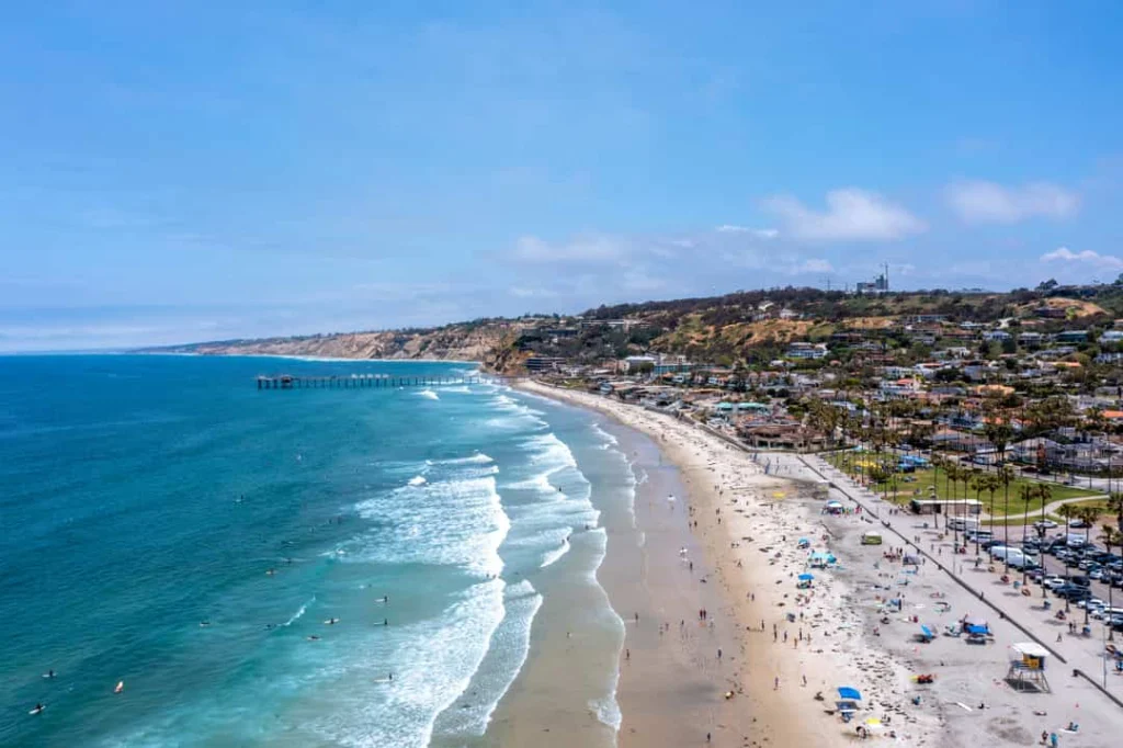 Luchtfoto van een zandstrand vol strandgangers bij San Diego met heldere zee, een pier in de verte en huizen langs de boulevard